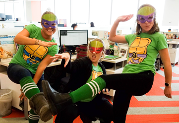 Three women dressed up like Teenage Mutant Ninja Turtles in an office cubicle