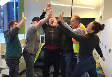 Seven people in hoodies and reflective vests high fiving in a circle