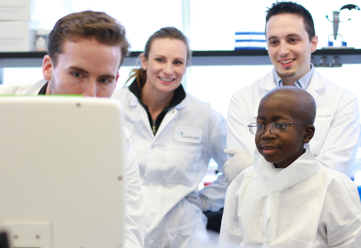 Three scientists in a lab showing a young boy data on a computer screen