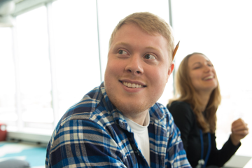 A man smiling looking to the right while a woman laughs in the background
