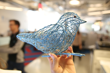 A hand holding a blue bird figurine up with an office setting in the background