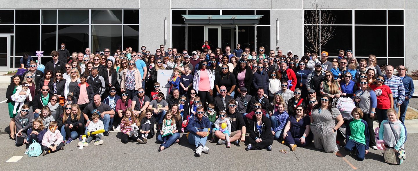 Large group of adults and children posing and wearing sunglasses.