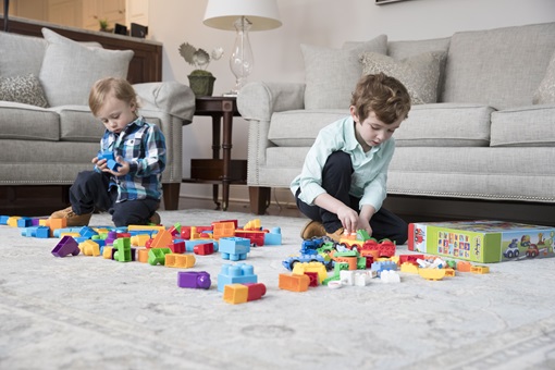 Two young boys playing with brightly colored stacking blocks on a living room floor
